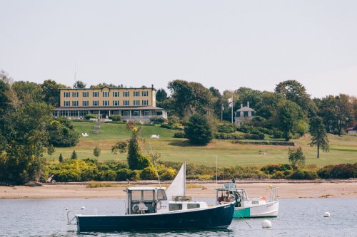 Two boats in the foreground with a yellow building and green landscape in the background on a calm waterway.
