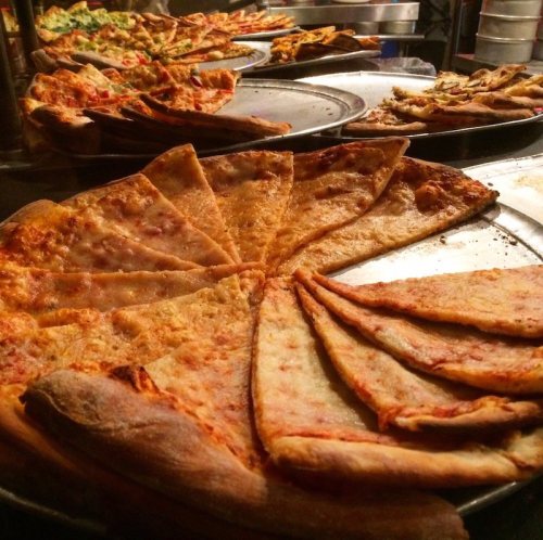 A variety of pizza slices on trays, showcasing different toppings and crust styles in a casual dining setting.
