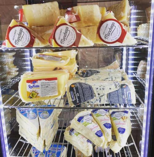 A display case filled with various types of cheese, including wedges of raclette and blue cheese.