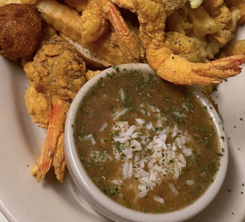 A plate of fried shrimp and vegetables with a small bowl of rice and gravy, garnished with herbs.