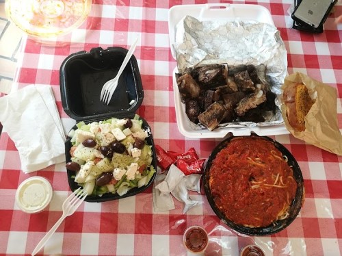 A checkered tablecloth with a salad, ribs, spaghetti with sauce, and a hot dog, accompanied by utensils and condiments.