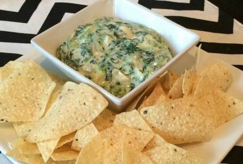 A bowl of creamy spinach dip surrounded by crispy tortilla chips on a patterned tablecloth.