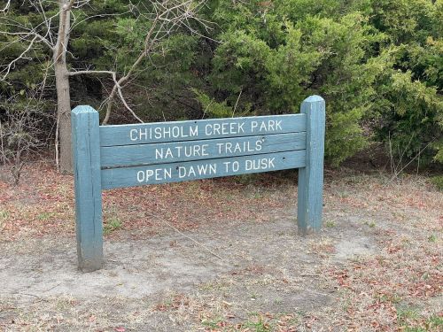 Sign for Chisholm Creek Park Nature Trails, stating "Open Dawn to Dusk," surrounded by greenery.
