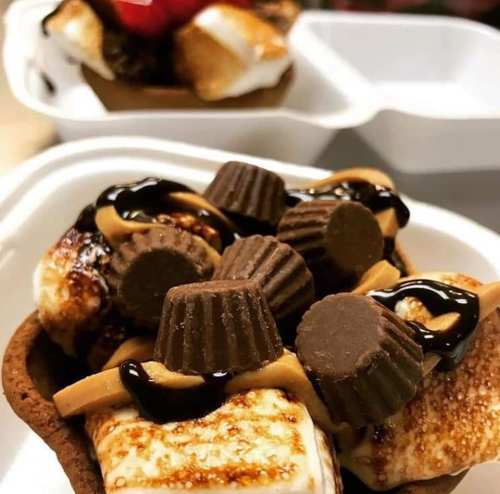A dessert bowl with toasted marshmallows, chocolate drizzle, and mini peanut butter cups on a chocolate crust.