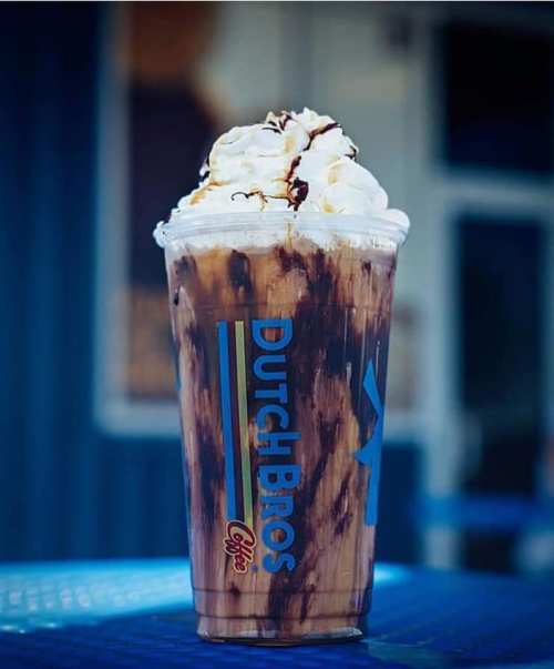 A frosty drink from Dutch Bros topped with whipped cream and chocolate drizzle, set against a blue background.