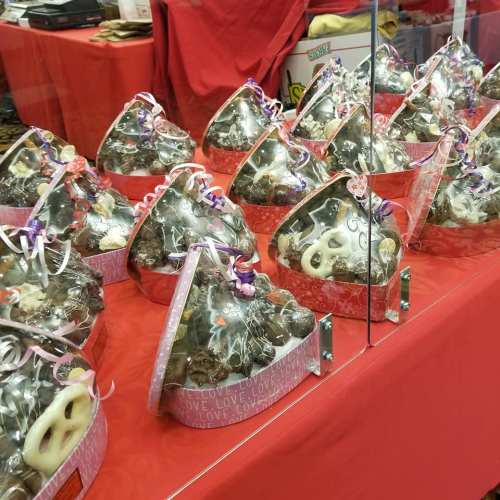 A display of heart-shaped gift boxes filled with treats, decorated with ribbons, on a red tablecloth.