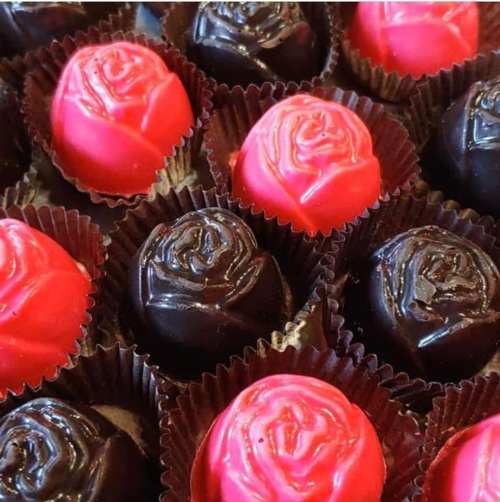 A close-up of chocolate rose-shaped candies in red and black, arranged in paper cups.