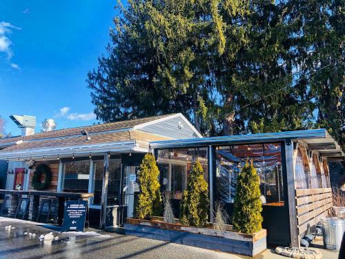 A cozy restaurant with outdoor seating, surrounded by trees and blue skies, featuring a wooden deck and festive decor.