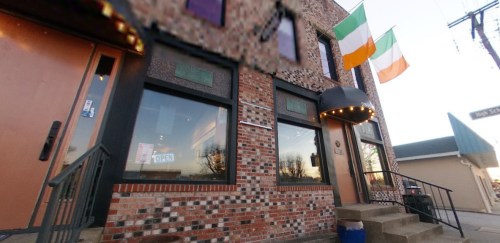 Exterior of a brick building with an awning, featuring Irish flags and an "Open" sign in the window.