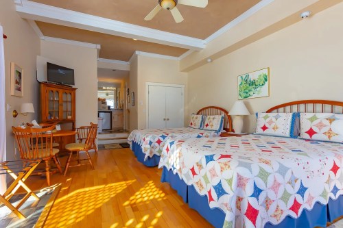 Cozy hotel room with two beds, a dining table, and a kitchenette area, featuring warm wood floors and bright decor.