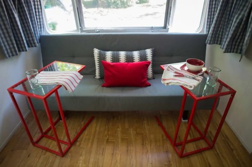 Cozy seating area with a gray couch, red pillows, and modern red side tables with glasses and bowls.