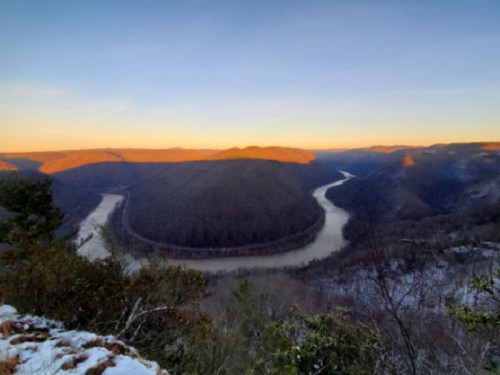 A scenic view of a winding river surrounded by mountains at sunset, with a clear sky and snow on the ground.