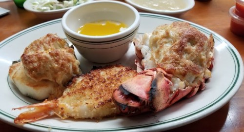 A plate featuring a lobster tail, crab cakes, and a small bowl of melted butter.