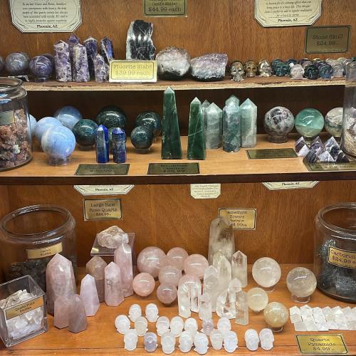 Display of various crystals and gemstones on wooden shelves, including spheres, towers, and polished stones.