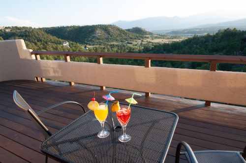 Two colorful cocktails on a table with a scenic view of mountains and valleys in the background.