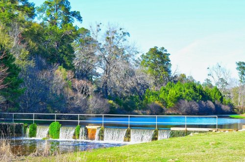 A serene landscape featuring a small dam with flowing water, surrounded by lush greenery and trees under a clear blue sky.
