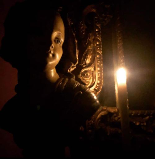 A dimly lit statue of a child beside a flickering candle, casting soft shadows on an ornate mirror.