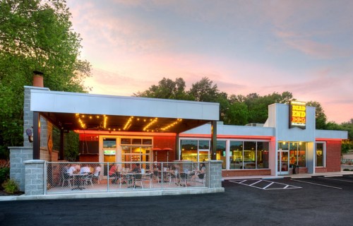 Exterior view of a restaurant at sunset, featuring outdoor seating and a bright sign that reads "Dead End BBQ."