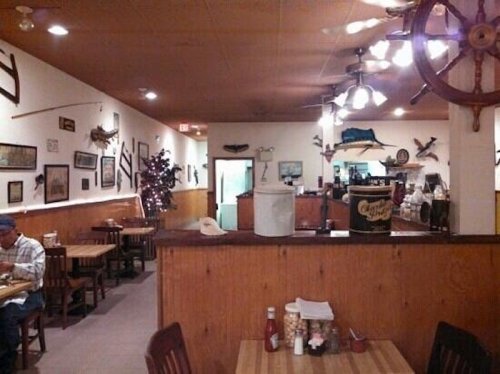 Cozy restaurant interior with wooden tables, nautical decor, and a festive tree in the corner.