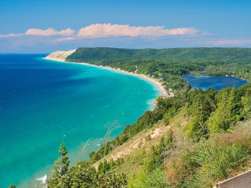 A scenic view of a coastline with turquoise waters, sandy beaches, and lush green hills under a clear blue sky.