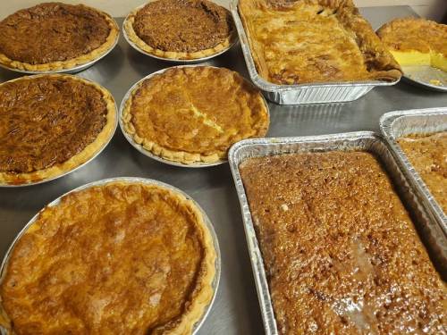 A variety of freshly baked pies and desserts on a metal surface, including pecan and pumpkin pies.