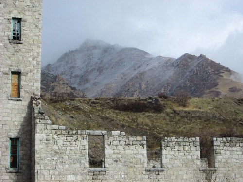 A crumbling stone wall in the foreground with misty mountains rising in the background under a cloudy sky.