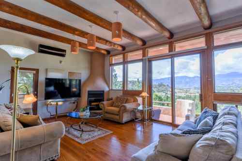 Cozy living room with wooden beams, large windows, and a view of mountains, featuring comfortable seating and a TV.