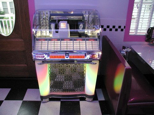 A vintage jukebox with colorful lights, located in a retro diner setting with black and white checkered flooring.