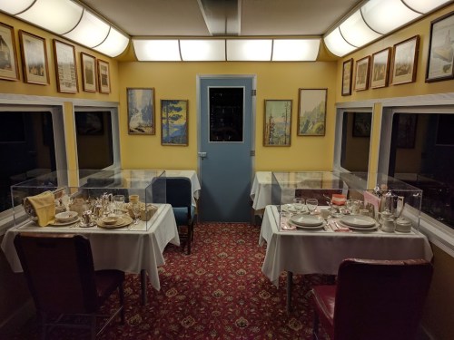 A cozy dining area with two elegantly set tables, surrounded by framed artwork and warm yellow walls.