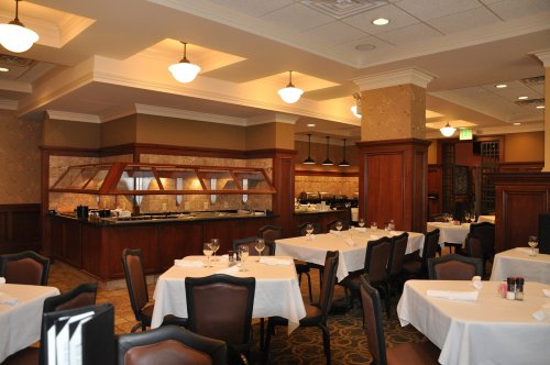 Elegant restaurant interior with white tablecloths, wooden accents, and a buffet area in the background.