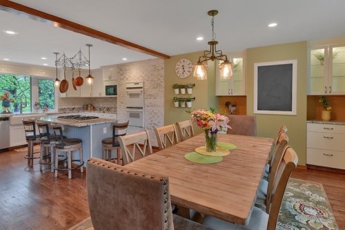 A modern kitchen and dining area with a wooden table, chairs, and decorative lighting, featuring green accents and a chalkboard.