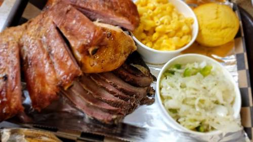 A platter featuring sliced smoked meat, macaroni and cheese, cornbread, and a side of coleslaw.