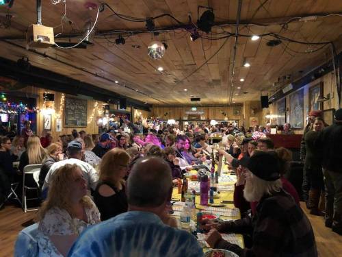 A crowded restaurant with people dining at long tables, decorated with lights and a lively atmosphere.