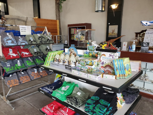 A display of colorful T-shirts, books, and toys in a shop, featuring dinosaur and fossil themes.