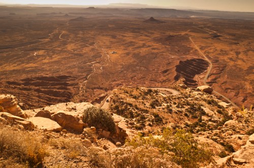 A vast desert landscape with rocky terrain, winding roads, and distant mountains under a clear sky.