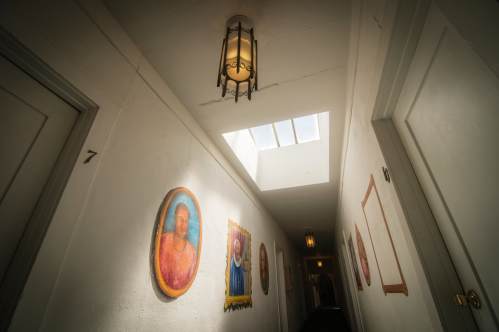 A hallway with white walls, framed portraits, and a skylight, illuminated by a hanging light fixture.