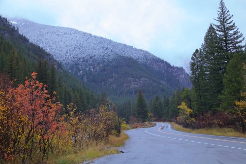 A winding road through a mountainous landscape with autumn foliage and snow-capped peaks in the background.