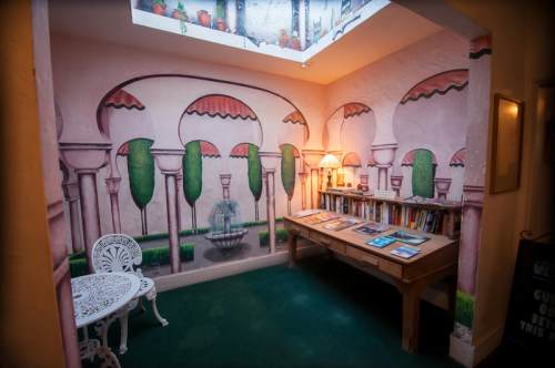 Cozy reading nook with a mural of arches and greenery, featuring a table of books and a white chair.