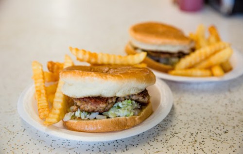 Two plates with sandwiches and crinkle-cut fries on a speckled table. One sandwich is partially visible.