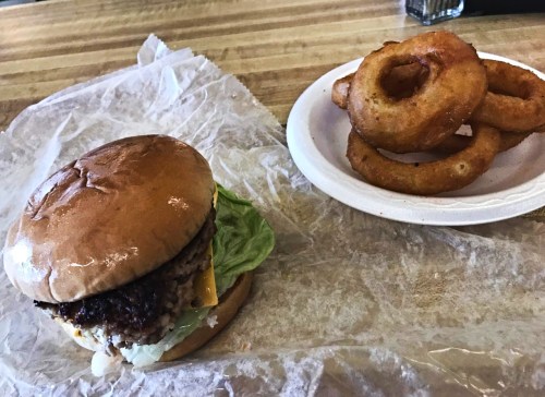 A hamburger with lettuce and cheese on a bun, next to a plate of crispy onion rings.