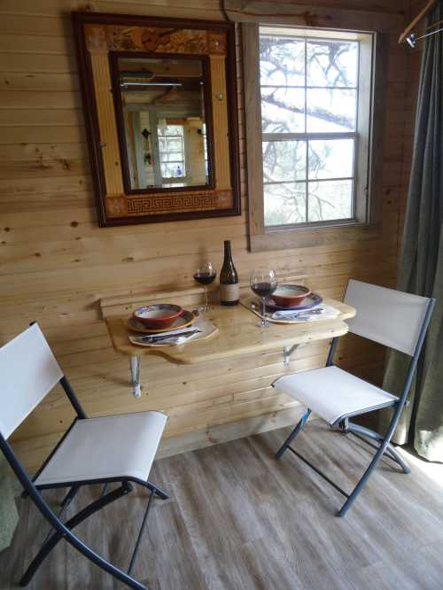 A cozy dining nook with a wooden table set for two, featuring wine glasses and a bottle, against a wooden wall.