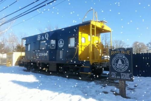 A blue and yellow caboose sits on snowy ground, with a sign nearby reading "Royal Blue" and details about the B&O Railroad.