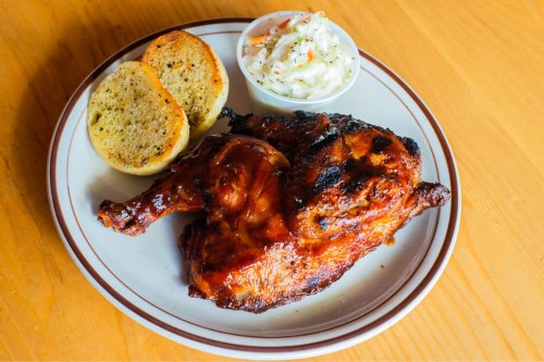A plate featuring grilled chicken with barbecue sauce, two slices of garlic bread, and a side of coleslaw.