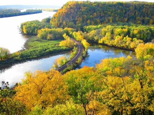 A scenic view of a winding river surrounded by vibrant autumn foliage and rolling hills.