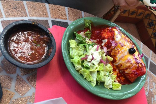 A plate of enchiladas topped with sauce, served with a side of salad and a small bowl of salsa.