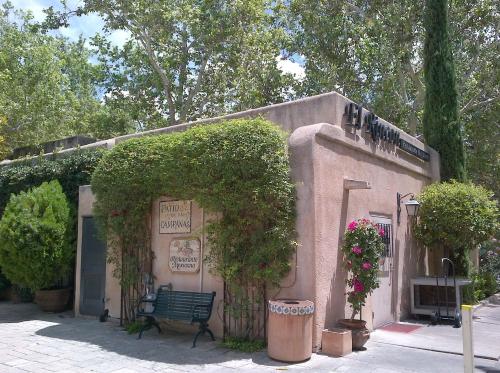 A charming adobe-style building surrounded by greenery and flowers, featuring a sign for a restaurant.