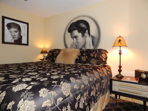 A bedroom featuring a floral-patterned bedspread, Elvis-themed decor, and a vintage lamp beside the bed.