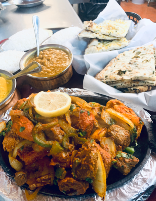 A sizzling platter of spiced meat with onions and peppers, served with rice, lentils, and flatbreads.