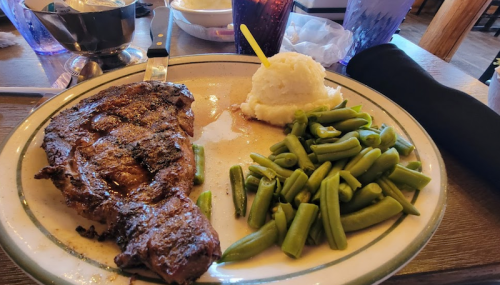 A plate with a grilled steak, mashed potatoes, and green beans, served in a casual dining setting.