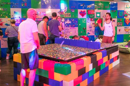 A colorful LEGO-themed space with people interacting, building, and playing at a large LEGO table.